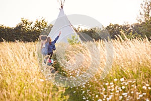 Two Female Friends Walking Pulling Trolley Through Field Towards Teepee On Summer Camping Vacation