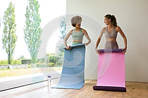 Two Female Friends Wearing Fitness Clothing Unrolling Exercise Mats In Gym Or Yoga Class