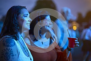 Two Female Friends Wearing Glitter Dancing At Outdoor Summer Music Festival Holding Drinks At Night