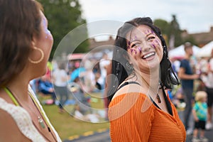 Two Female Friends Wearing Glitter Having Fun At Summer Music Festival Doing Cheers With Drinks