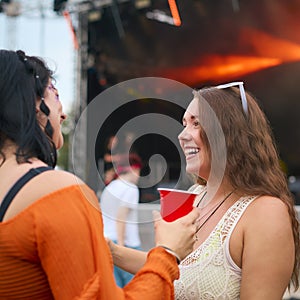 Two Female Friends Wearing Glitter Having Fun At Summer Music Festival Holding Drinks