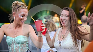Two Female Friends Wearing Glitter Having Fun At Summer Music Festival Holding Drinks
