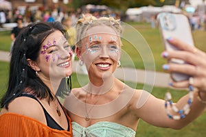 Two Female Friends Wearing Glitter Posing For Selfie At Summer Music Festival 