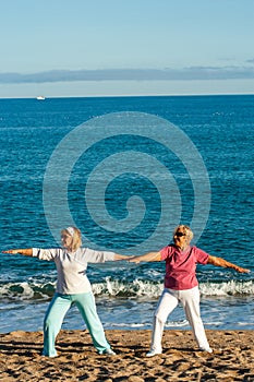 Two female golden agers doing yoga on beach. photo