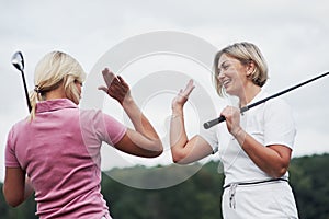 Two female golf players giving high five in the background of beautiful green woods