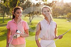Two Female Golfers Walking Along Fairway Carrying Clubs