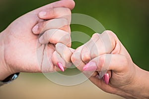 Two female hands friendship swear, holding little pinkie finger together.closeup, shallow depth of field. focused. blurred green b