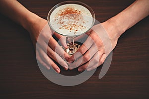 Two female hands hold a glass of eggnog on wooden table background