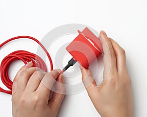 Two female hands are holding a cable and a red box with wireless headphones