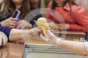Two female hands holding with fruit ice cream cone, seller giving ice cream to customer. Real scene in store