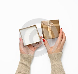 Two female hands holding a square golden gift box with a bow on a white background, concept of gratitude, birthday