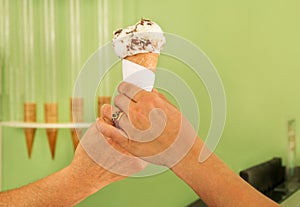 Two female hands holding a vanilla with chocolate ice cream cone. Woman sells ice cream in pastry shop.