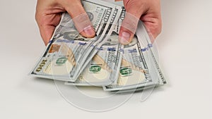 Two female hands are laying on a white table a stack of paper hundred US dollar bills