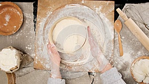 Two female hands sift white wheat flour through a round wooden sieve on the table