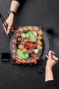 Two female hands using chopsticks to take rolls from sushi set