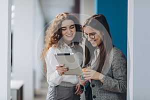 Two female managing directors discussing ideas of project on digital tablet while walking down in office hall, confident women