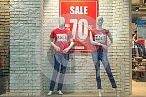Two female mannequins in red T-shirts and blue jeans in a shop window against a background of a white brick wall