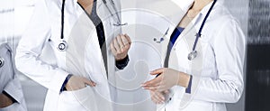 Two female physicians are discussing medical therapy, while standing at the table in a clinic office. Doctors use pc