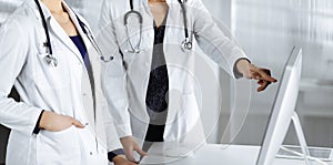 Two female physicians are discussing medical therapy, while standing at the table in a clinic office. Doctors use pc