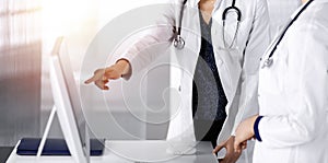 Two female physicians are discussing medical therapy, while standing at the table in a clinic office. Doctors use pc