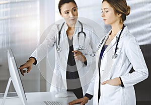 Two female physicians are discussing medical therapy, while standing at the table in a sunny clinic office. Doctors use