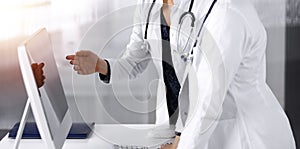 Two female physicians are discussing medical therapy, while standing at the table in a sunny clinic office. Doctors use