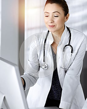 Two female physicians are discussing medical therapy, while standing at the table in a sunny clinic office. Doctors use