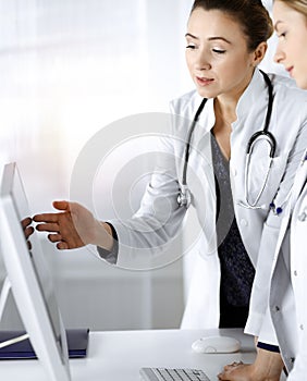 Two female physicians are discussing medical therapy, while standing at the table in a sunny clinic office. Doctors use