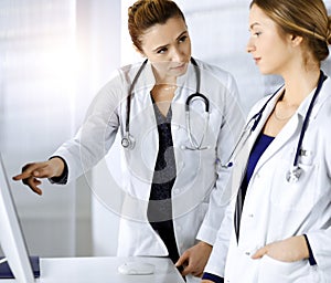 Two female physicians are discussing medical therapy, while standing at the table in a sunny clinic office. Doctors use