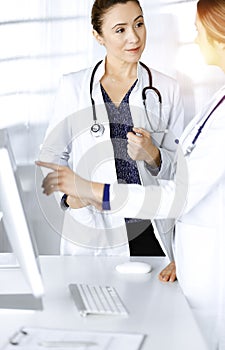 Two female physicians are discussing medical therapy, while standing at the table in a sunny clinic office. Doctors use