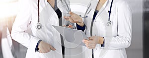 Two female physicians are discussing medical therapy, while standing at the table in a sunny clinic office. Doctors use