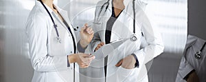 Two female physicians are discussing their patient`s medical tests, while standing in a clinic office. Doctors use a