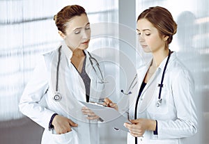 Two female physicians are discussing their patient's medical tests, while standing in a clinic office. Doctors use a