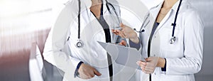 Two female physicians are discussing their patient`s medical tests, while standing in a sunny clinic office. Doctors use