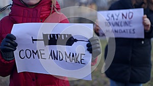 Two female protestors with Come and make banner and Say no to vaccine mandates banners outdoors. Unrecognizable