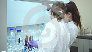 Two female researchers discuss flasks beaker with transparent liquid on desk. Spbd scientist study