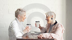 Two female senior collegues sitting next to each other in an cafe