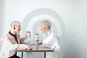 Two female senior collegues sitting next to each other in an cafe