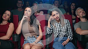 Two female spectators watching uninteresting film unpleasant face expression sleeping auditorium