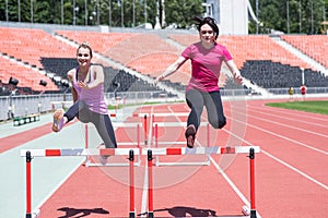 Two female sportswomen are jumping over an obstacle. Running with hurdles. Active lifestyle.