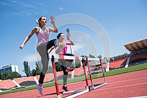 Two female sportswomen are jumping over an obstacle. Running with hurdles. Active lifestyle.