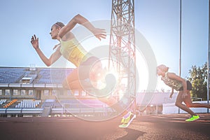 Two female sprinter athletes running on the treadmill race during training in athletics stadium.