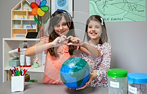 Two female students showing globe world earth while one making heart shape with hands