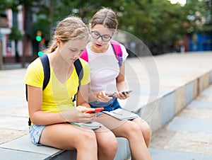 Two female students use phones to check lessons and write down completed assignments in notebook