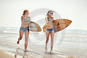 Two female surfers running on the beach holding surfboards