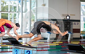 Two female swimmers taking the start position and jumping in a pool
