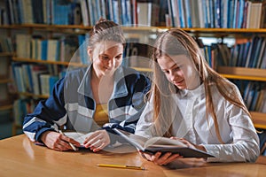 Two female teenagers chatting while studying in a school library