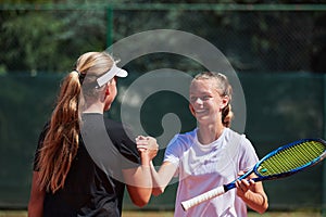 Two female tennis players shaking hands with smiles on a sunny day, exuding sportsmanship and friendship after a