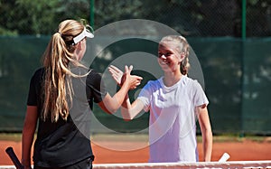 Two female tennis players shaking hands with smiles on a sunny day, exuding sportsmanship and friendship after a