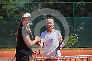 Two female tennis players shaking hands with smiles on a sunny day, exuding sportsmanship and friendship after a